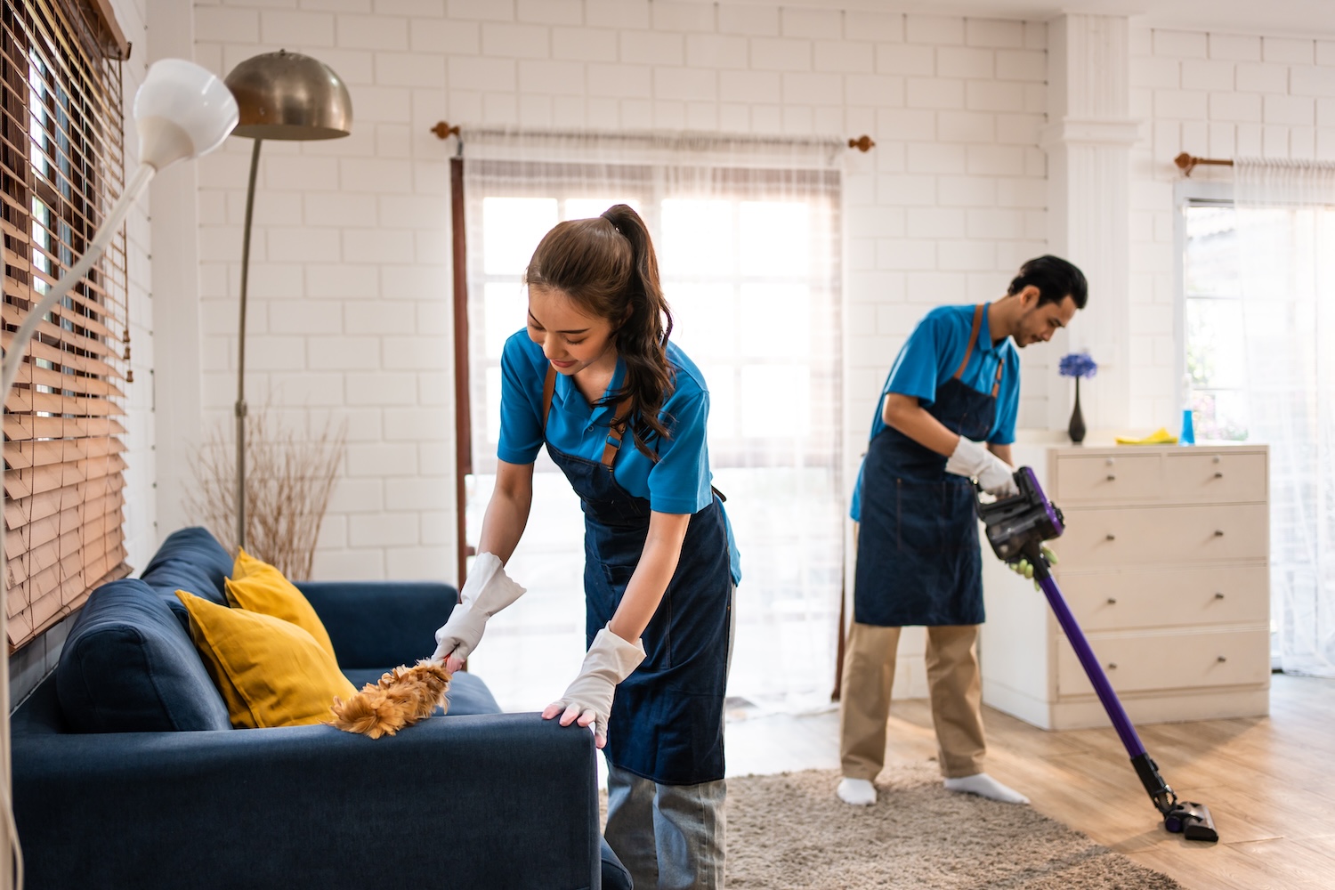 Asian young man and woman cleaning service worker work in living room. Attractive housekeeper cleaner team wear apron and cleaning messy dirty floor for housekeeping housework and chores in house. Home Maintenance Services in Westminster
